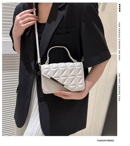 Close-up of white quilted handbag with gold metal bar accent on a black blazer