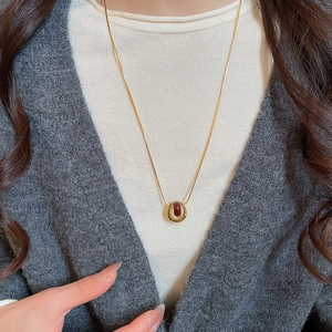 Close-up of gold-plated U-shaped pendant with a dark red bead on a snake chain
