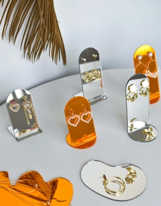 Macro view of arched mirror and orange acrylic earring display stand with dried palm leaf