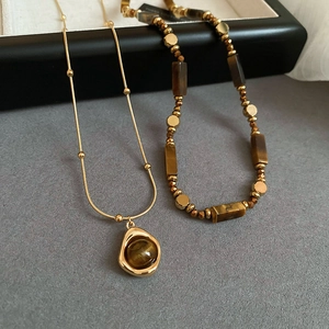 Detail of gold-plated tiger eye beaded necklace set with geometric pendants on grey fabric