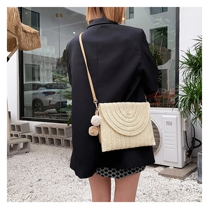 Handwoven cream straw bag with flap cover, decorative pom-poms and leather shoulder strap