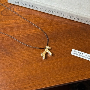 Detailed view of a golden poodle pendant on a black cord over a rustic wooden table