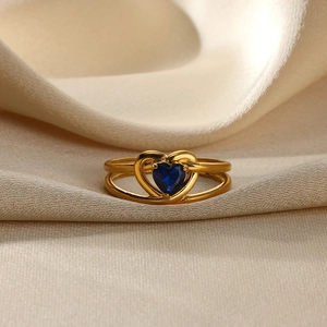 Macro shot of gold double-layer ring featuring a blue heart gemstone on beige silk fabric