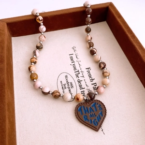 Detailed macro view of vintage beaded necklace with heart-shaped engraved charm on velvet tray