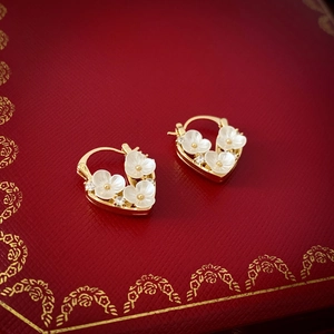Macro detail of gold heart earrings with white flower and zircon on red velvet box