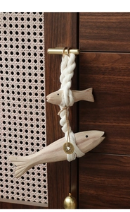 Detail of handcrafted wooden fish wall hanging with cotton rope and metallic bell accent