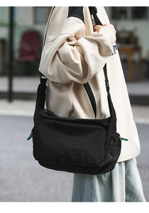 Close-up of black nylon messenger bag with green zipper cord detail on shoulder strap