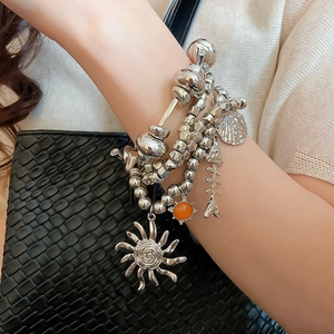 Detail of layered silver beaded bracelets with sun, shell and fishbone charms on wrist