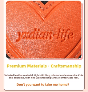 Macro detail of orange lychee grain leather heart keychain with embossed logo and stitching