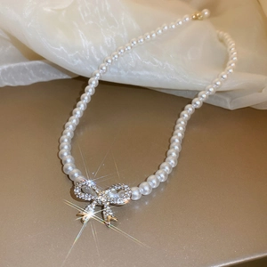 Detailed view of pearl necklace with rhinestone bow pendant on champagne silk background