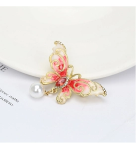 Detail of a gold butterfly brooch with red enamel wings, rhinestones and a hanging pearl