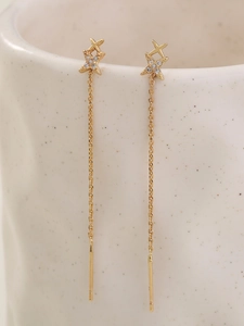 Macro shot of gold long tassel earrings with star zircon hanging on a ceramic cup