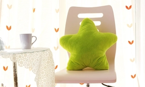Green star-shaped plush pillow on a white chair in a cozy, modern living room setting