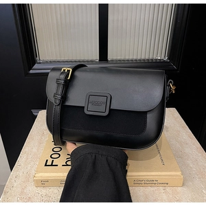 Close-up of black leather crossbody bag with mixed textures and gold logo clasp