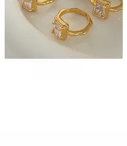 Macro detail of gold wavy rings with square clear zircon on a white reflective tray