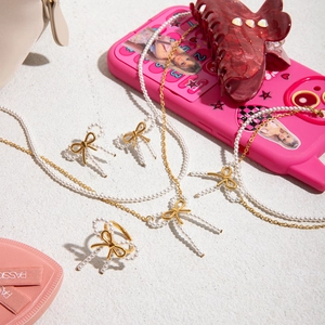 Chic golden bow jewelry set with white imitation pearls on a beige textured background