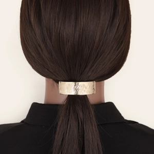 Textured gold rectangular metal hair clip securing a low ponytail on dark hair