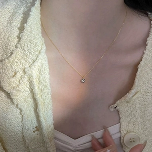 Close-up of a gold necklace with a circular pendant and black-white zircons on a model