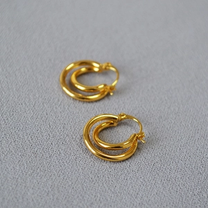 Detailed close-up of golden double hoop earrings with minimalist twisted design on grey cloth
