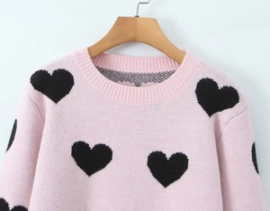 Close-up of pink knit sweater featuring black heart patterns and ribbed crew neck detail