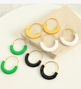 Detail of colorful enamel charms on gold hoop earrings displayed on a natural stone surface
