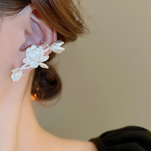 Close-up of a white lotus flower and leaf ear cuff worn by a model in soft lighting