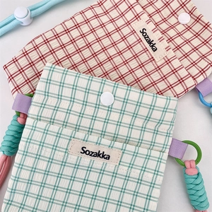 Detail of red and green plaid fabric pouches with snap button and woven lanyards