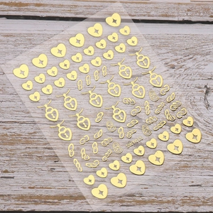 Détail d'autocollants dorés pour ongles avec motifs de cadenas cœur et chaîne