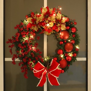 Christmas wreath with red berries, poinsettia flowers and warm LED lights on white window