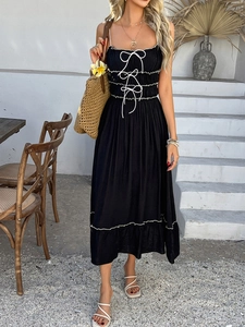 Detail of black camisole dress featuring white lace-up ties and ruffled hemline