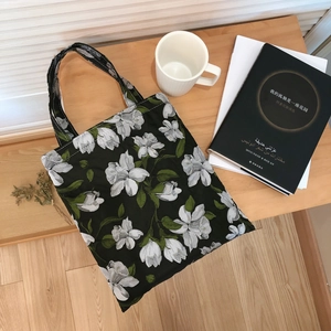 Floral black cotton handbag with white lilies and green leaves on a wooden table