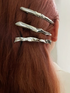 Close-up of three silver irregular wavy metal hair clips styled on red-brown hair