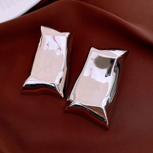 Macro shot of silver irregular wrinkled square metal earrings on dark velvet background
