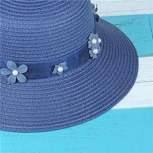Close-up of navy straw hat featuring intricate weaving and blue fabric flower with pearl