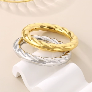 Detailed view of twisted rope rings in gold and silver finish on a wavy stand