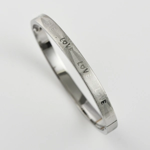 Macro detail of silver stainless steel bangle featuring etched wave texture and LOVE engraving