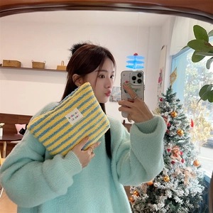 Close-up of yellow and blue striped plush makeup bag with woven label detail