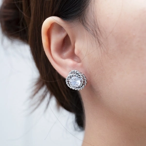 Close-up of a silver knot stud earring with a central round zircon on the earlobe