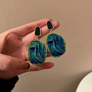 Macro detail of resin drop earrings with deep teal stone texture and gold metal edges