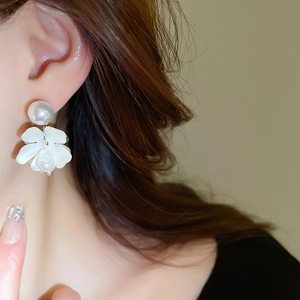 Close-up of elegant flower and pearl stud earrings on model with soft lighting