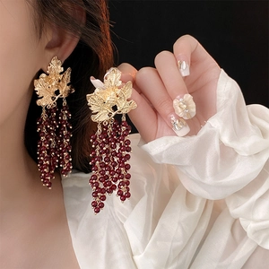 Detail of vintage gold leaf earrings with dark red beaded tassels on a model
