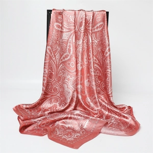 Gros plan d'un foulard carré en satin rose à motif paisley blanc sur un support