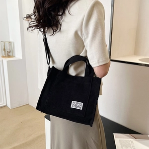 Black corduroy tote bag with front pocket shown in a lifestyle shoulder carry view
