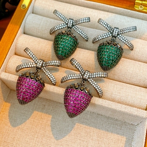 Macro shot of strawberry earrings with zircon bowknot inlay on beige jewelry display