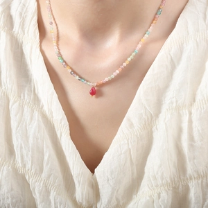 Colorful beaded gemstone necklace with red agate drop pendant on a woman's neck