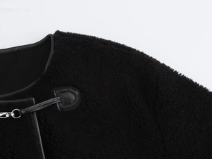 Gros plan d'une veste en fourrure noire avec passepoil en cuir et boucles métalliques