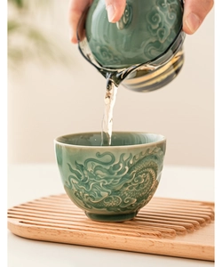 Close-up of pouring tea into a celadon cup featuring a delicate 3D dragon relief pattern