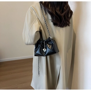 Detail of black glossy drawstring bag with gold chain strap and elegant pearl charm