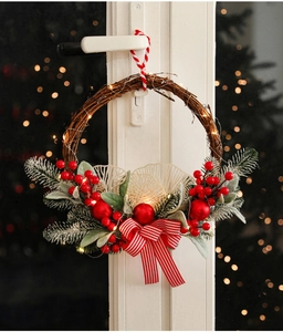 Detail of Christmas wreath with red berries, pine cones and warm LED lights on a door