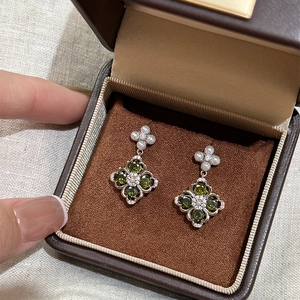 Detailed view of silver flower earrings with green stones and pearls in a jewelry box